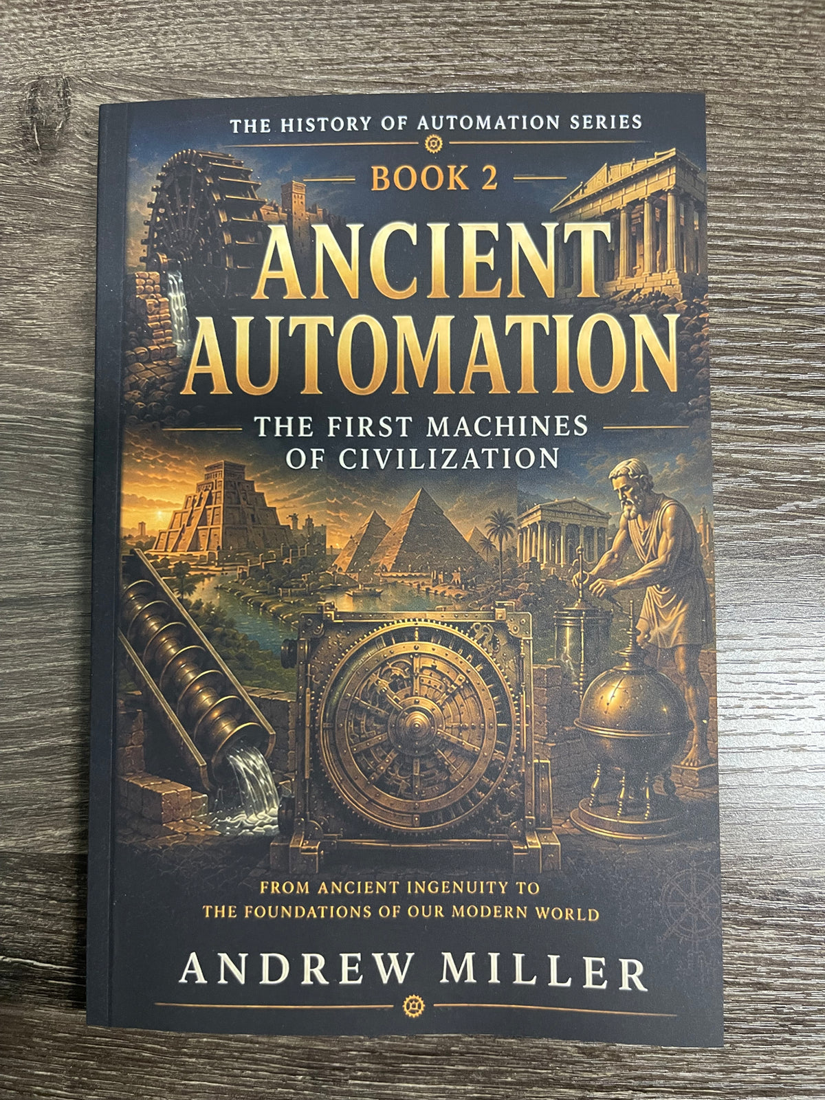 The book 'Ancient Automation: The First Machines of Civilization' by Andrew Miller, Book 2 in 'The History of Automation Series', displayed flat on a dark wood background.
